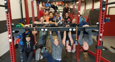 Adults participating in a strength workout while hanging from a Rogue rig at City Fit Shop, a family fitness gym in Edmonton.