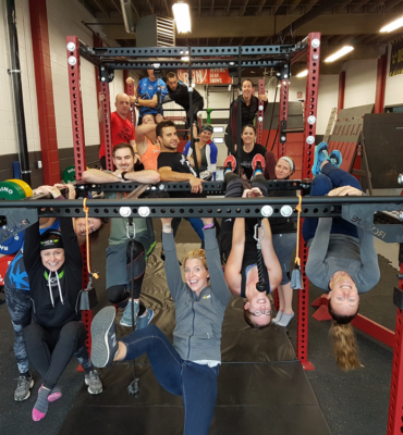 Adults participating in a strength workout while hanging from a Rogue rig at City Fit Shop, a family fitness gym in Edmonton.